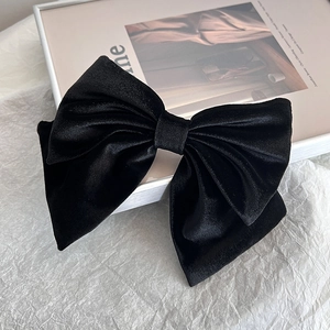 Close-up of elegant black silk velvet large bow hair clip on a minimalist white background
