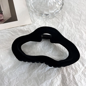 Detail of black flocked hair claw clip with wave design on textured background