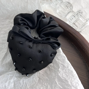 Close-up of black satin scrunchie with beaded heart bow on elegant wooden tray