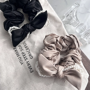 Elegant satin bow scrunchies with pearls in black and champagne on canvas background