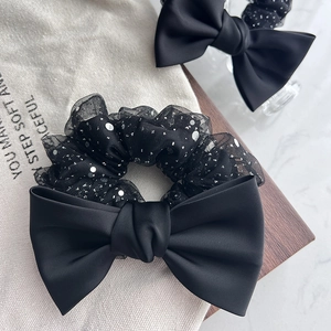 Detail view of a black bow scrunchie with glitter mesh on a wooden tray with accessories