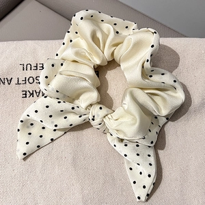 Detailed macro shot of a cream satin bow scrunchie with black polka dots on canvas