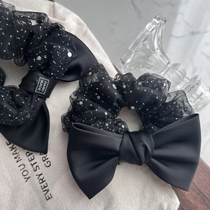 Elegant black satin bow scrunchie with sequined mesh and a handmade label on marble