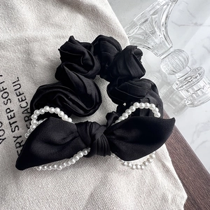 Close-up of black satin hair scrunchie with large bow and white pearl trim details