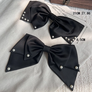 Elegante große schwarze Satin-Haarschleifen mit weißen Perlen auf neutralem Stoffhintergrund