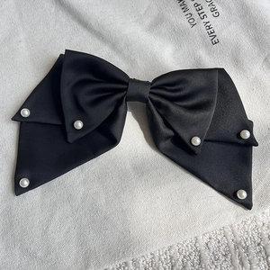 Close-up of black satin bow hair clip with elegant pearls on textured white background
