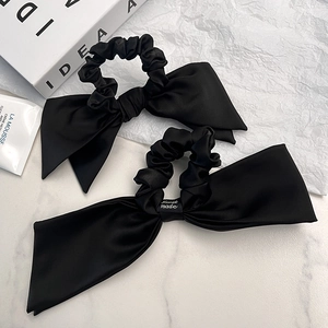 Elegant black satin bow scrunchie with handmade label on a minimalist marble background