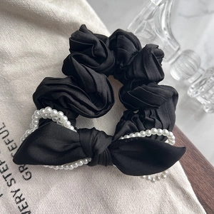 Elegant black satin scrunchie with large bow and double-row pearl detailing shown from a side view