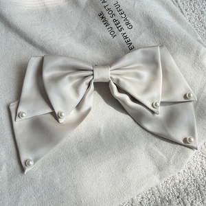 Close-up of elegant champagne satin bow hair clip with pearls on a textured background