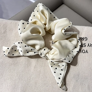 Detailed macro view of cream satin scrunchie with black polka dots and chic bow tie ribbon