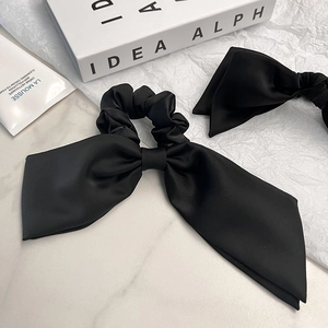 Detail of two black satin bow scrunchies on white marble with silk gloss texture