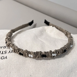 Détail d'un serre-tête en satin plissé champagne orné de perles et de strass noirs élégants