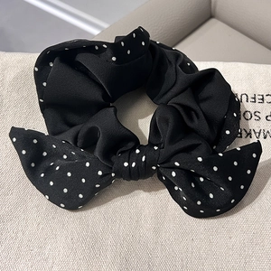Elegant black polka dot silk scrunchie with a large bow tie on neutral background