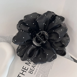 Détail d'une grande pince à cheveux fleur en satin noir avec strass sur un magazine