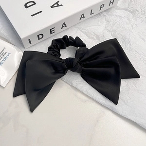 Elegant black satin oversized bow hair scrunchie shown on a minimalist white background