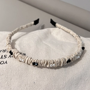 Détail d'un serre-tête en satin plissé beige orné de perles et de fleurs noires