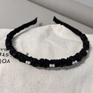 Détail d'un serre-tête en satin plissé noir avec des perles sur un fond en toile blanche