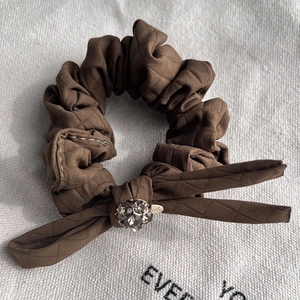Detail of a brown quilted fabric hair scrunchie with a bow and faceted grey crystal bead