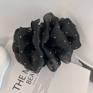 Détail d'un chouchou en organza noir orné de strass argentés sur un fond élégant