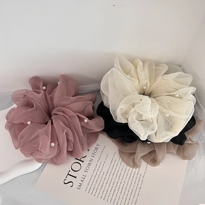 Detail of large mesh hair scrunchies with pearls in beige, black, and pink colors