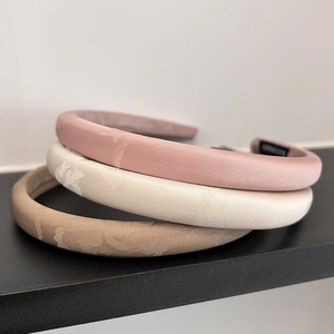 Close-up of three jacquard satin padded headbands in pink, beige, and khaki colors
