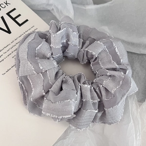 Macro detail of light grey hair scrunchie with pleated texture and raw fringe edges
