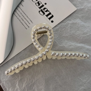 Detail view of cream white hair claw clip with faux pearls and rhinestones on gray paper
