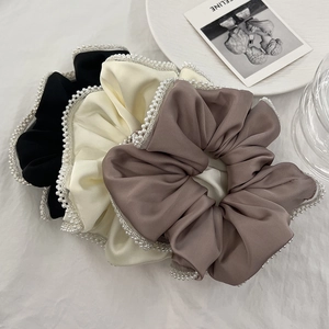 Detailed macro of large satin hair scrunchies with white pearl edges in three soft colors