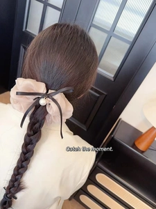 Dettaglio dell'elastico scrunchie in organza champagne con fiocco nero e perla nei capelli