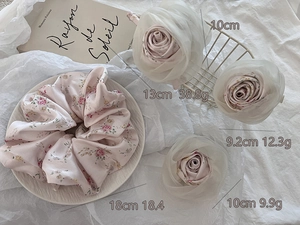 Detailed view of pink floral satin hair scrunchie and white sheer fabric rose clips