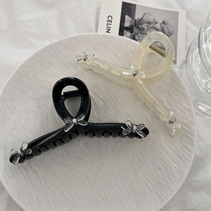 Elegant set of black and beige acrylic hair claws with decorative bow details on a tray