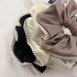 Close-up of three satin hair scrunchies in black, beige, and brown with pearl trim edge