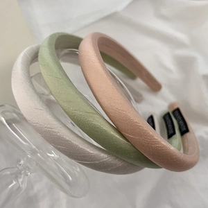 Detail of three satin-textured handmade headbands in pearl white, sage green, and soft pink