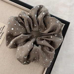 Close-up of a beige velvet scrunchie featuring elegant rhinestones on a textured background