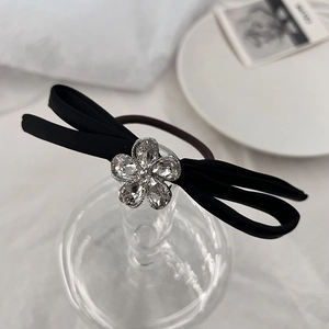 Detailed close-up of a black satin bow hair tie with a sparkling crystal flower center