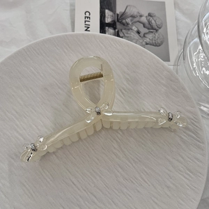 Detail of cream resin hair claw clip with bow embellishment and golden metal spring