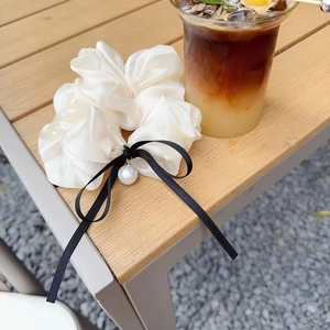 Dettaglio dello scrunchie bianco perla effetto seta con fiocco nero e perla