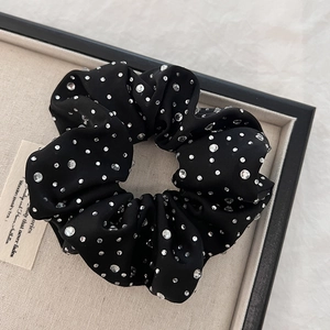 Macro detail of black satin scrunchie with sparkling white rhinestones on linen tray