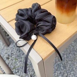 Dettaglio di uno scrunchie in seta nera con perla bianca e un elegante fiocco di nastro