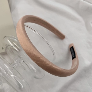 Detail view of light pink satin headband with handmade label on white fabric