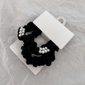 Détail de chouchous en tissu noir avec perles blanches sur une carte de présentation