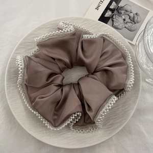 Detail of coffee brown silk satin scrunchie with pearl mesh lace trim on a white plate