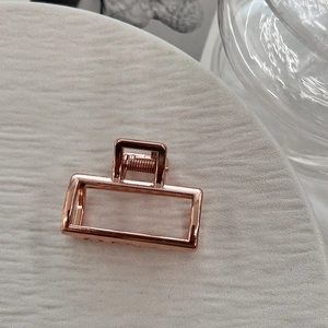 Close-up of a rectangular rose gold alloy hair claw clip with a sleek hollowed-out design