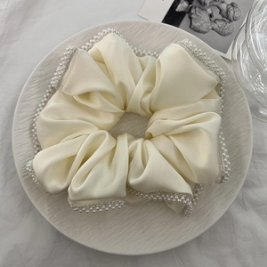 Close-up of a cream white satin oversized scrunchie with elegant faux pearl edges