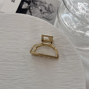 Detail of a minimalist gold alloy hair claw clip on a decorative stone surface