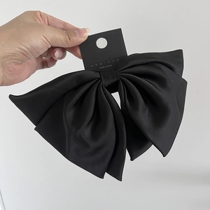 Detailed close-up of large black satin bow hair clip showing silk texture and spring clasp