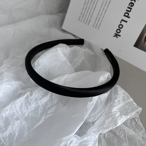 Detailed close-up of a padded black satin headband on a minimalist white paper background