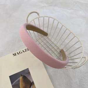 Détail d'un serre-tête rembourré rose crème sur un panier blanc montrant le fini satin