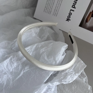 Detailed view of cream satin headband with smooth fabric texture on a fashion magazine