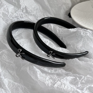 Close-up of glossy black patent headband featuring a silver metal bow detail ornament